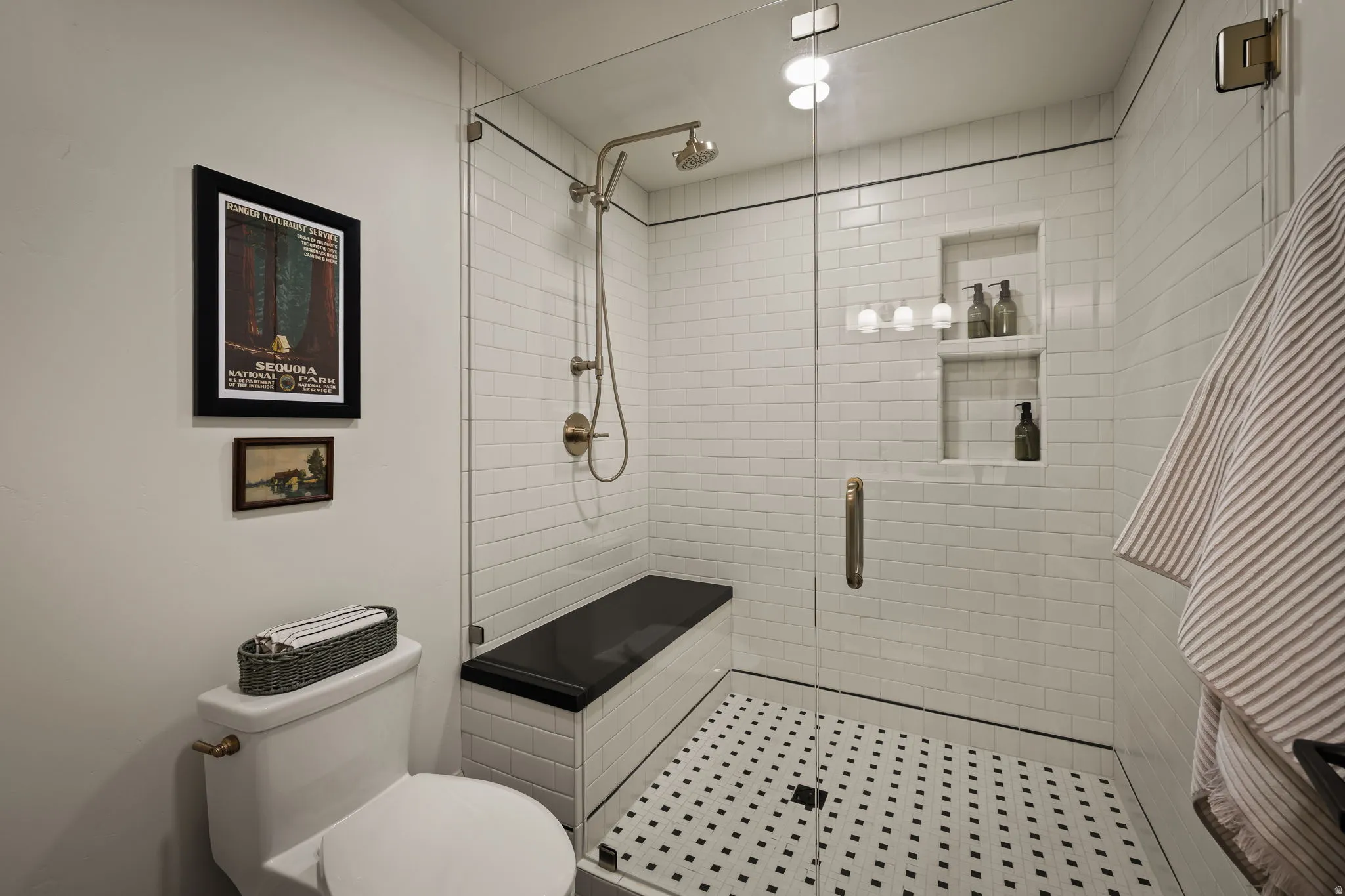 Glass-enclosed shower featuring white subway tile, a black and white mosaic tile floor, and a built-in black bench
