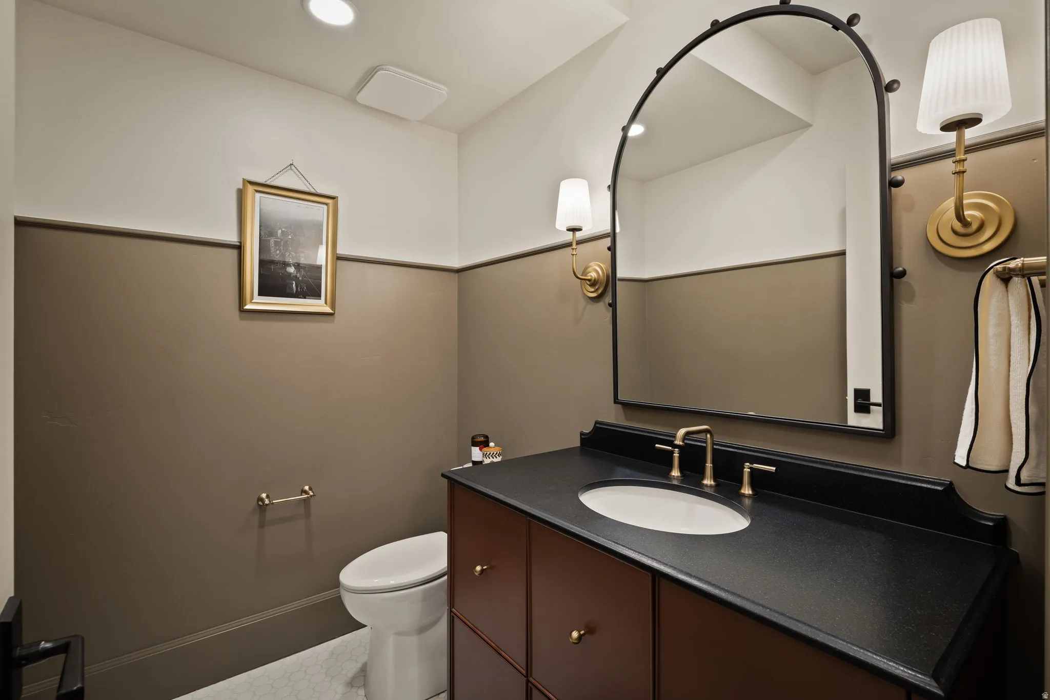 Bathroom featuring a dark wood vanity with a black countertop, oval undermount sink, and brass-finish faucet