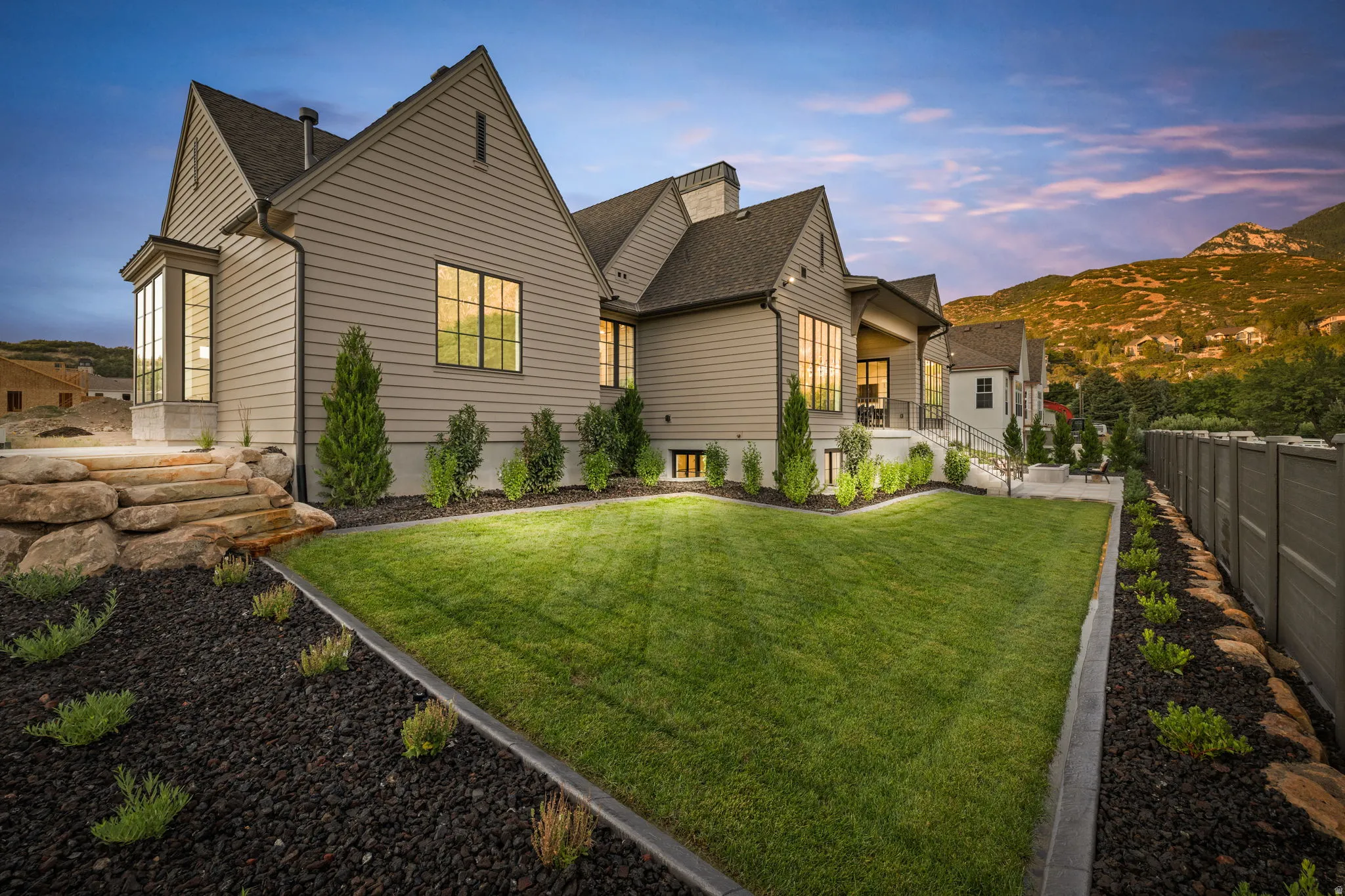 Expansive green lawn with integrated landscape lighting, complemented by a tiered rock retaining wall and decorative gravel beds