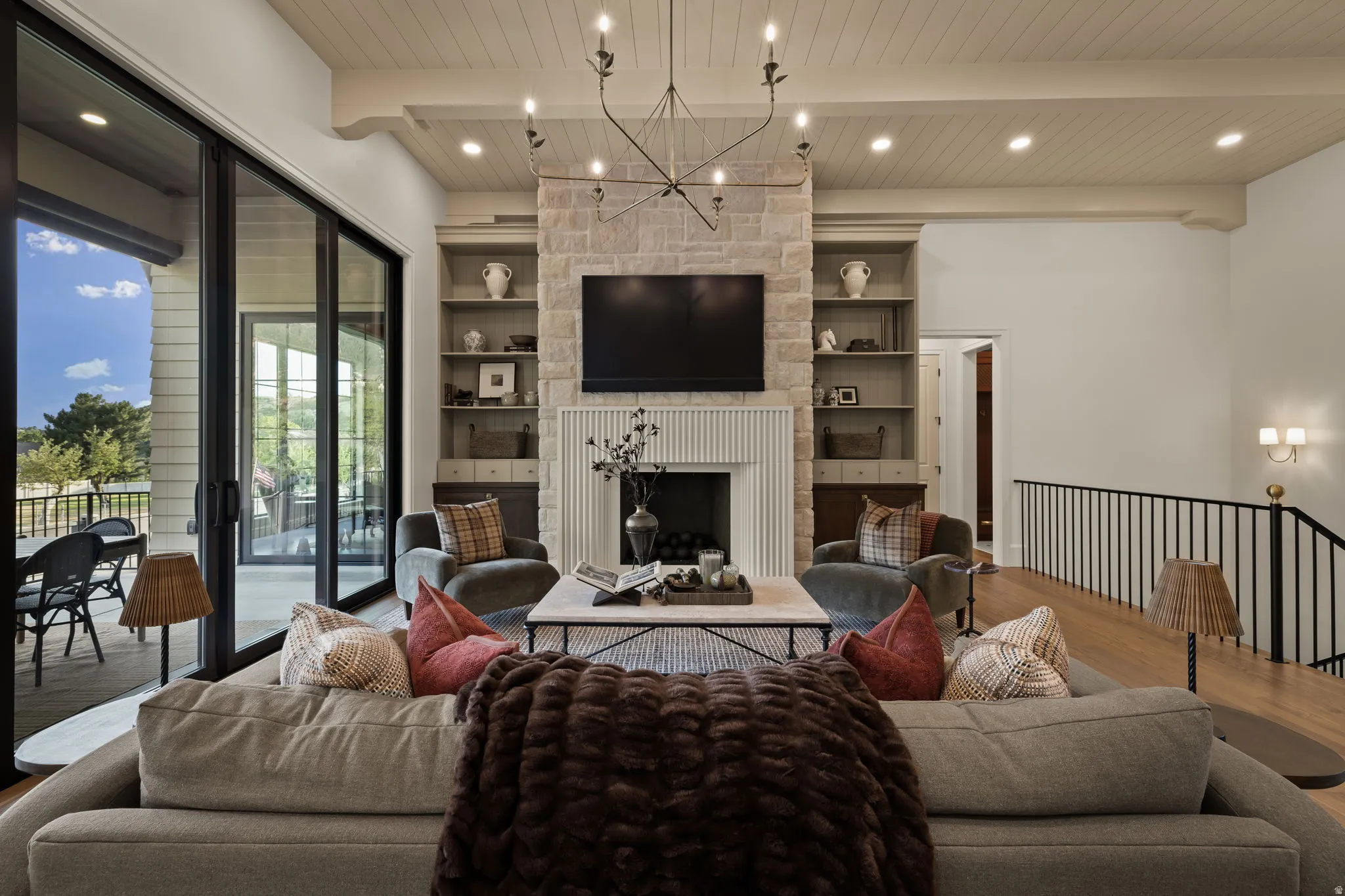 Living area featuring a stone-clad fireplace with reeded wood surround, integrated shelving with lower cabinetry, and wood-finish flooring