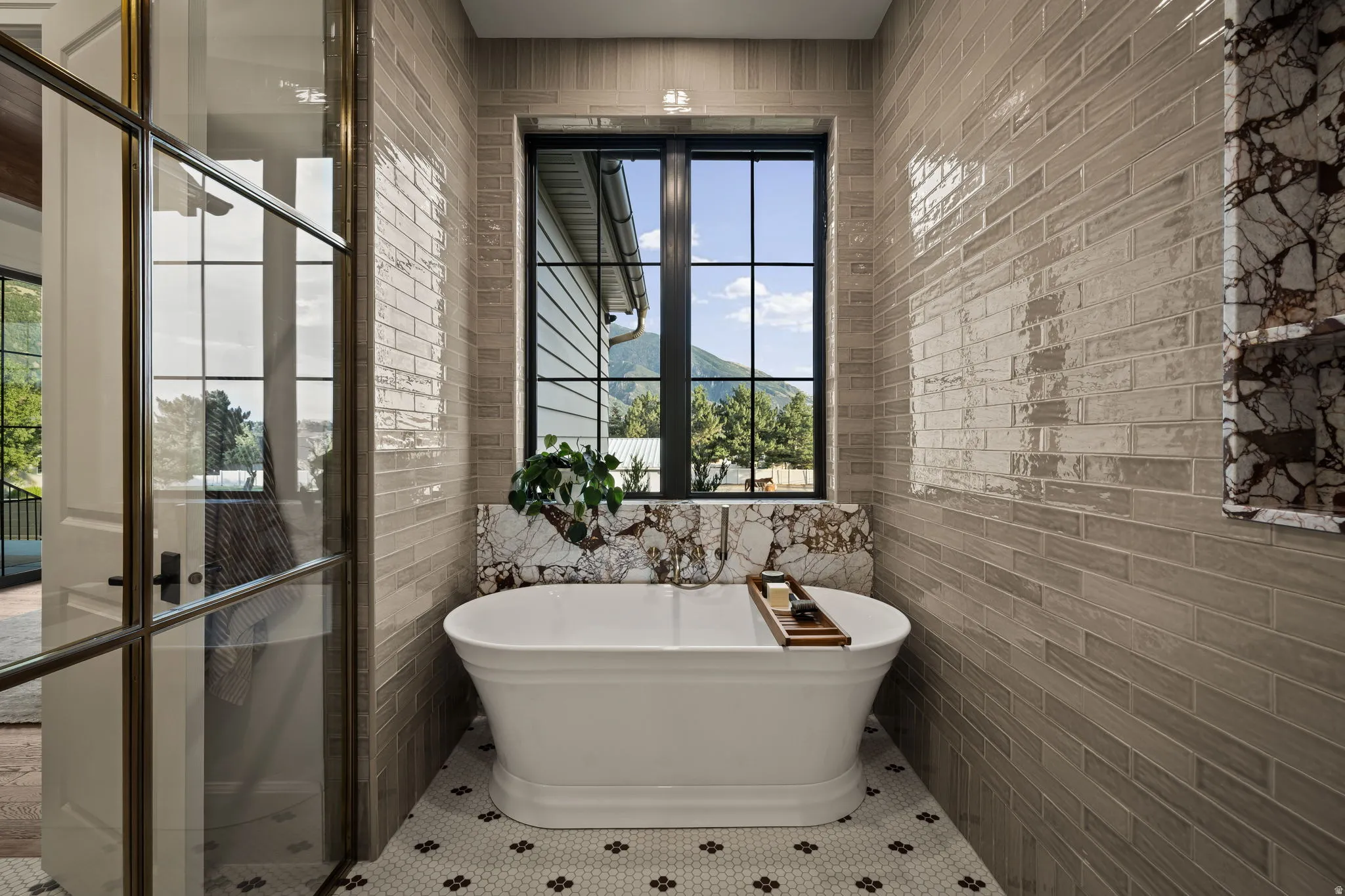 Freestanding tub with a natural stone surround and integrated shelf, complemented by a black-framed window