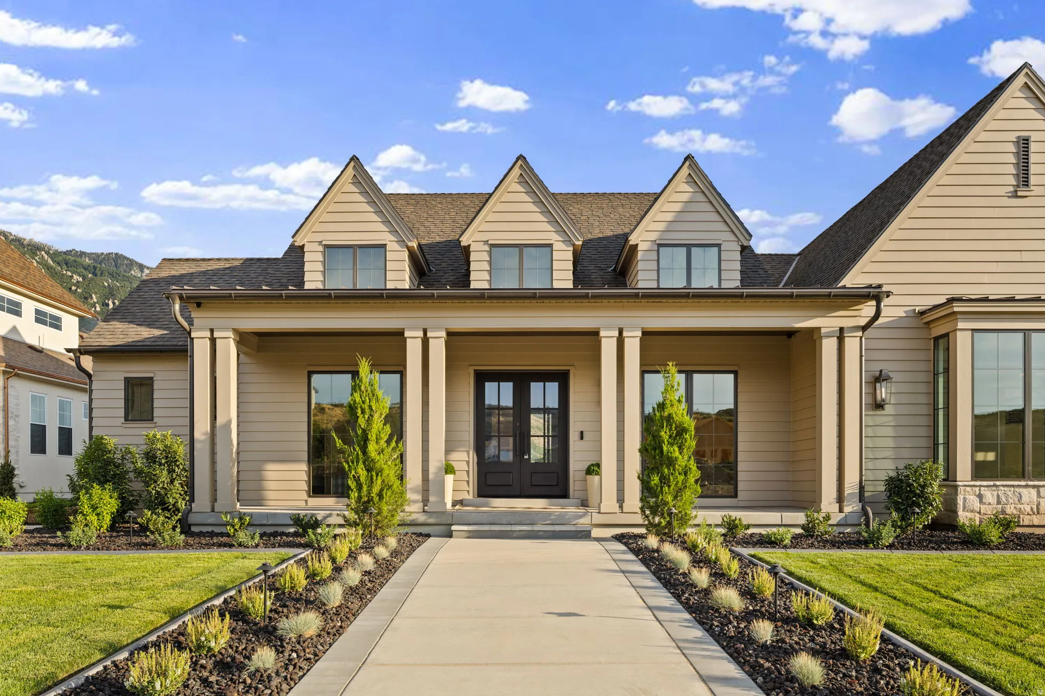 Craftsman-style home featuring a covered entry porch with substantial columns, dormer windows, and a black double-door entry