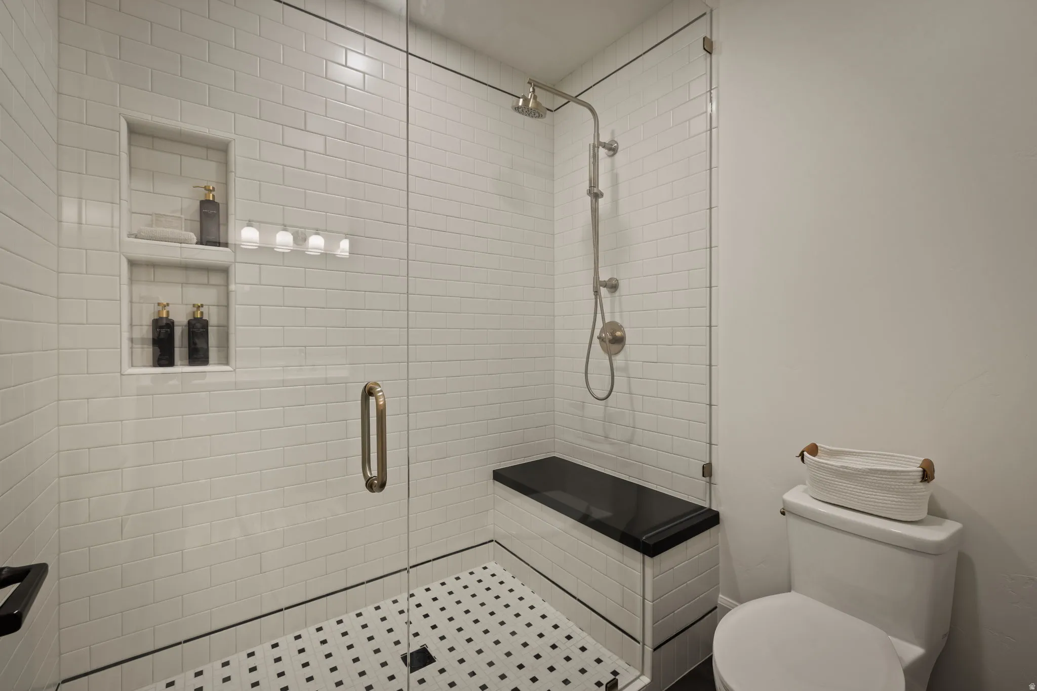Shower with subway tile walls, integrated shelving, and a black and white mosaic tile floor