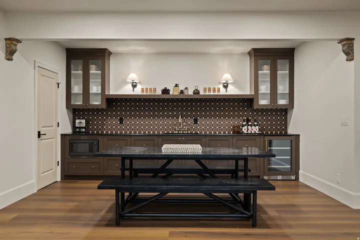 Integrated wet bar featuring rich brown cabinetry, dark countertops, and a patterned tile backsplash
