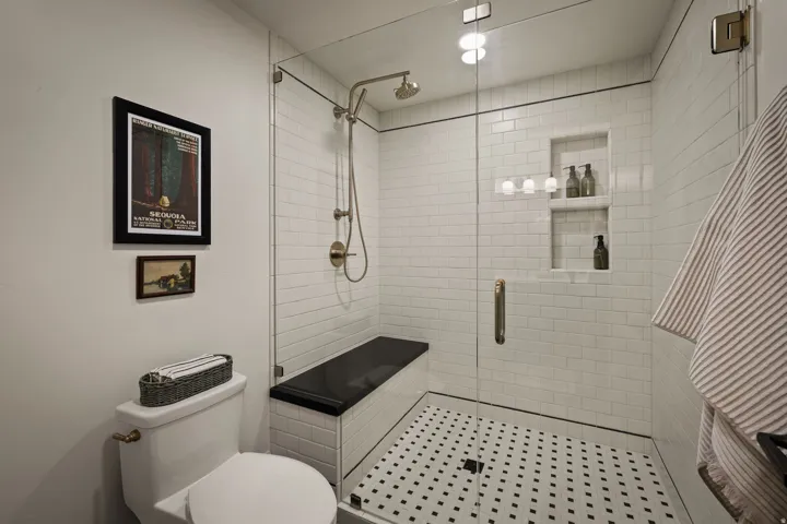 Glass-enclosed shower featuring white subway tile, a black and white mosaic tile floor, and a built-in black bench