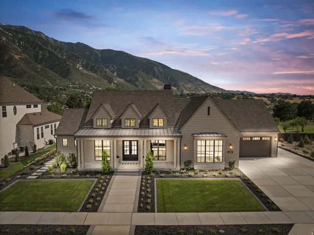Contemporary farmhouse exterior featuring dormer windows, a covered front porch, a bay window, an attached two-car garage, and a concrete driveway