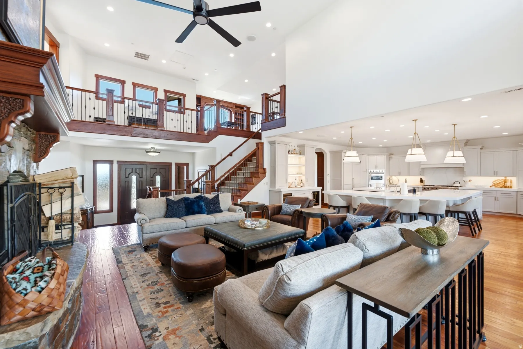 Great room featuring high ceilings, wood-finish flooring, a stone fireplace, and a two-story open layout with an upper-level balcony
