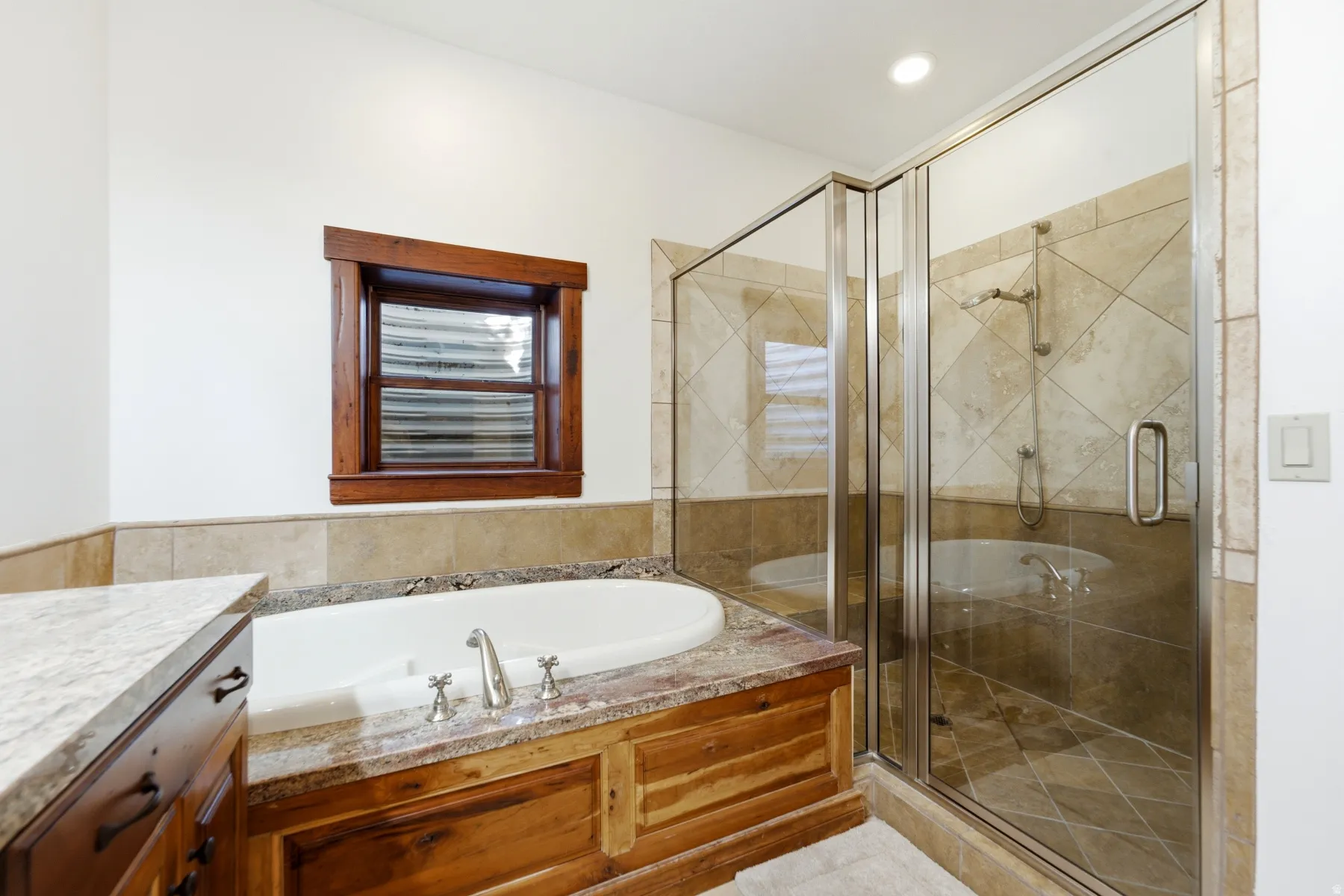 Bathroom featuring a built-in tub with a stone surround, a glass-enclosed shower with tiled walls, and a vanity with a stone countertop and wood cabinetry