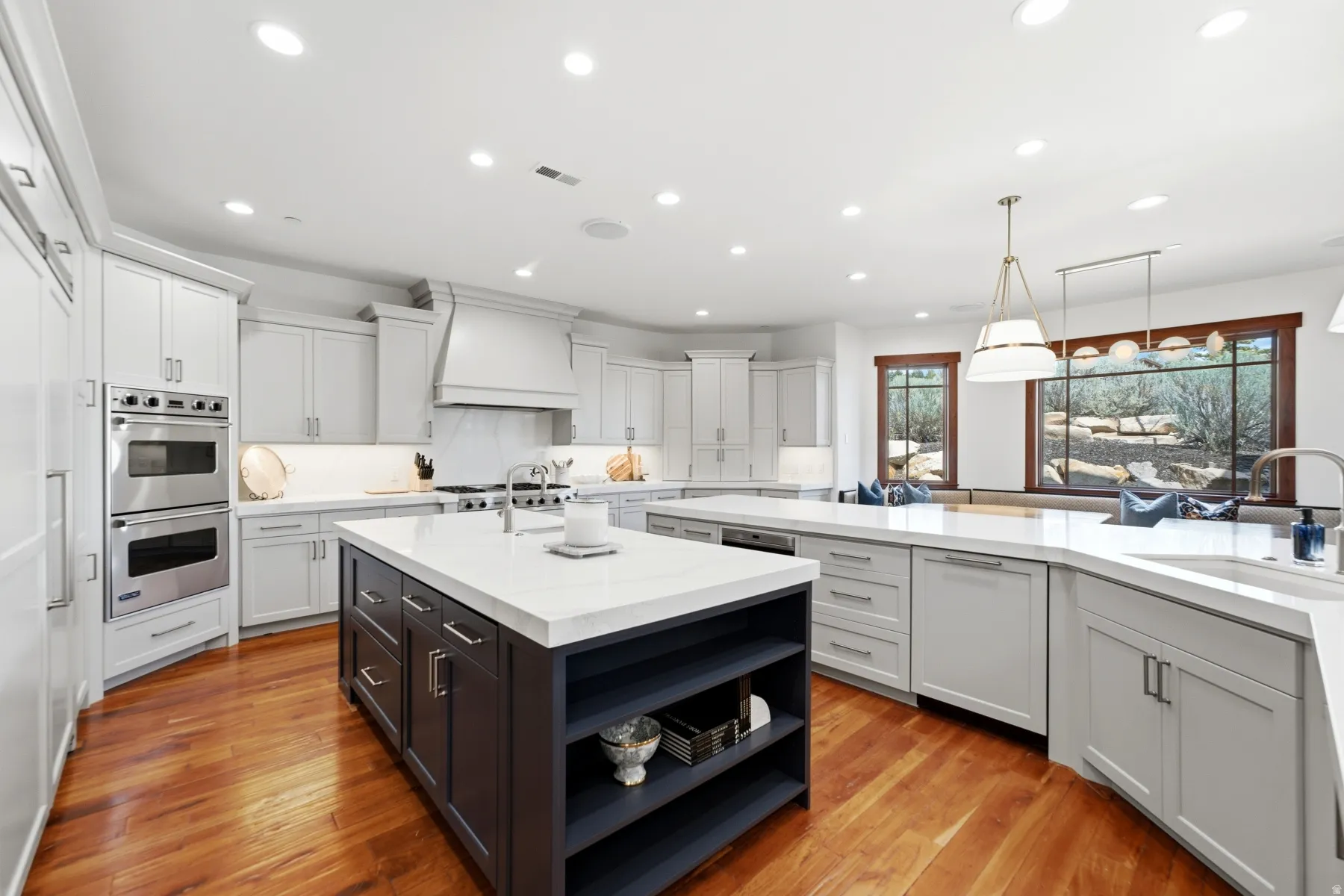 Spacious kitchen featuring two islands with stone countertops, integrated stainless steel appliances, light-toned cabinetry, and wood-finish flooring