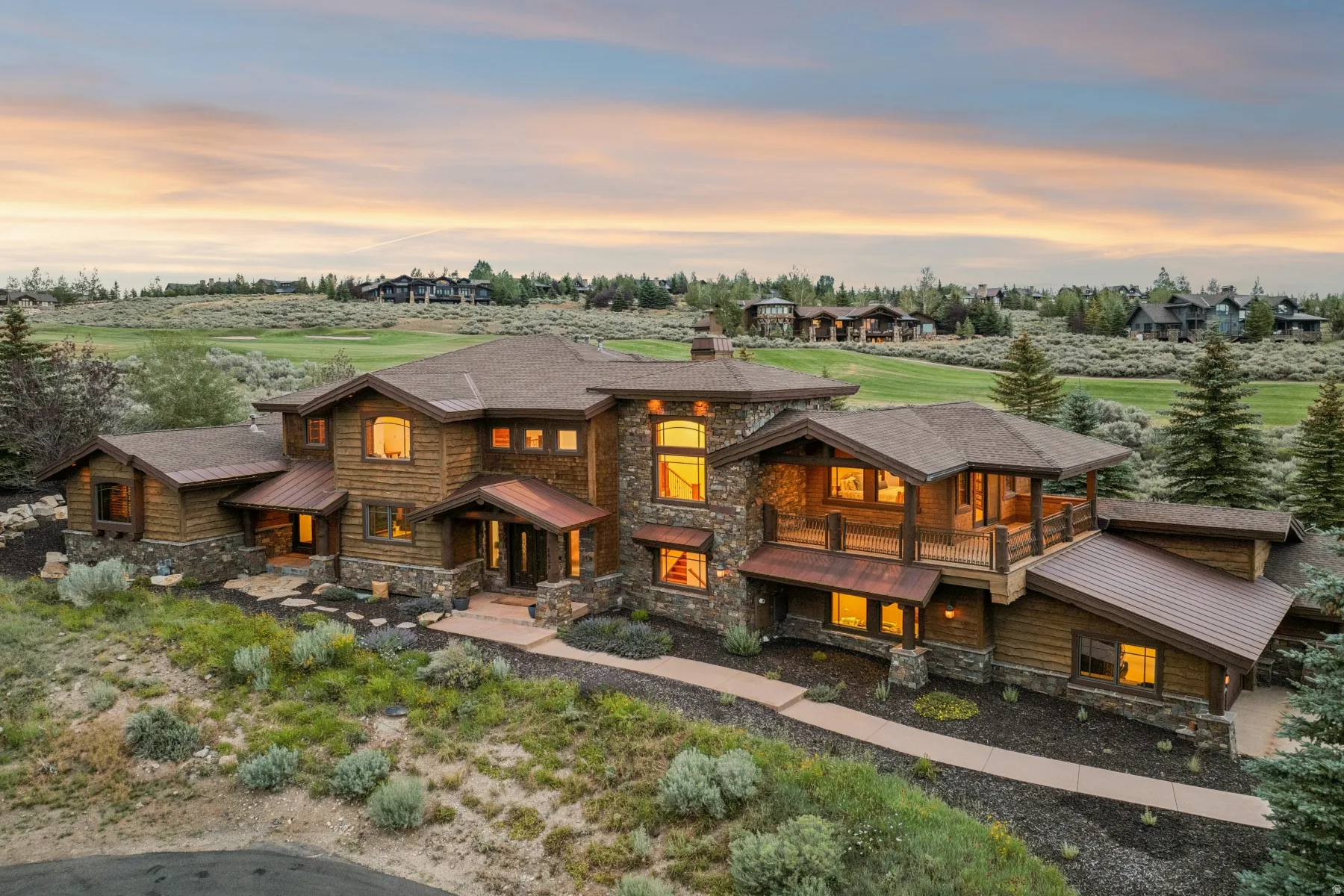 Expansive residence featuring a rustic wood and stone exterior, multiple balconies, a covered entry, an attached garage, and a landscaped pathway