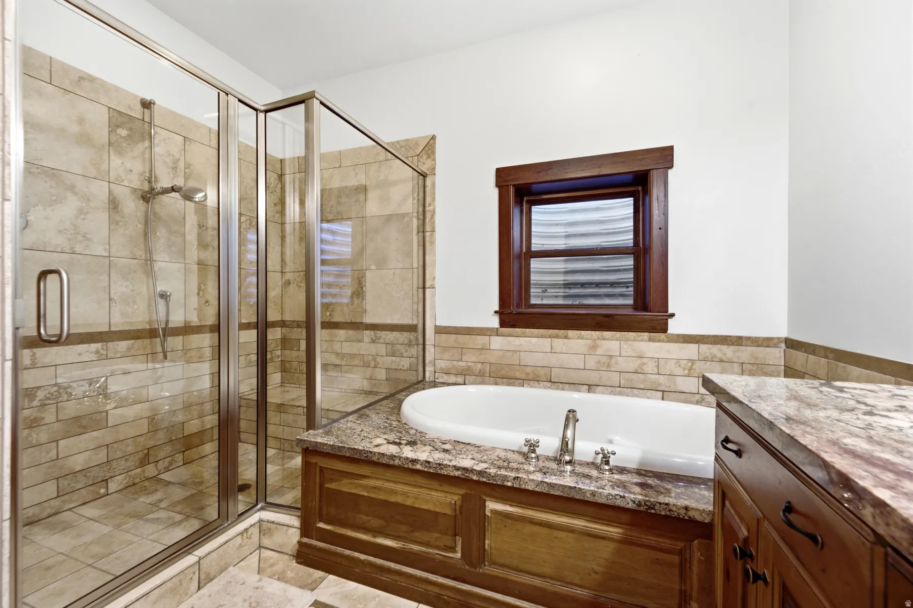 Spacious bathroom featuring a glass-enclosed shower with stone tile surround, a built-in soaking tub with a stone countertop, and custom wood cabinetry