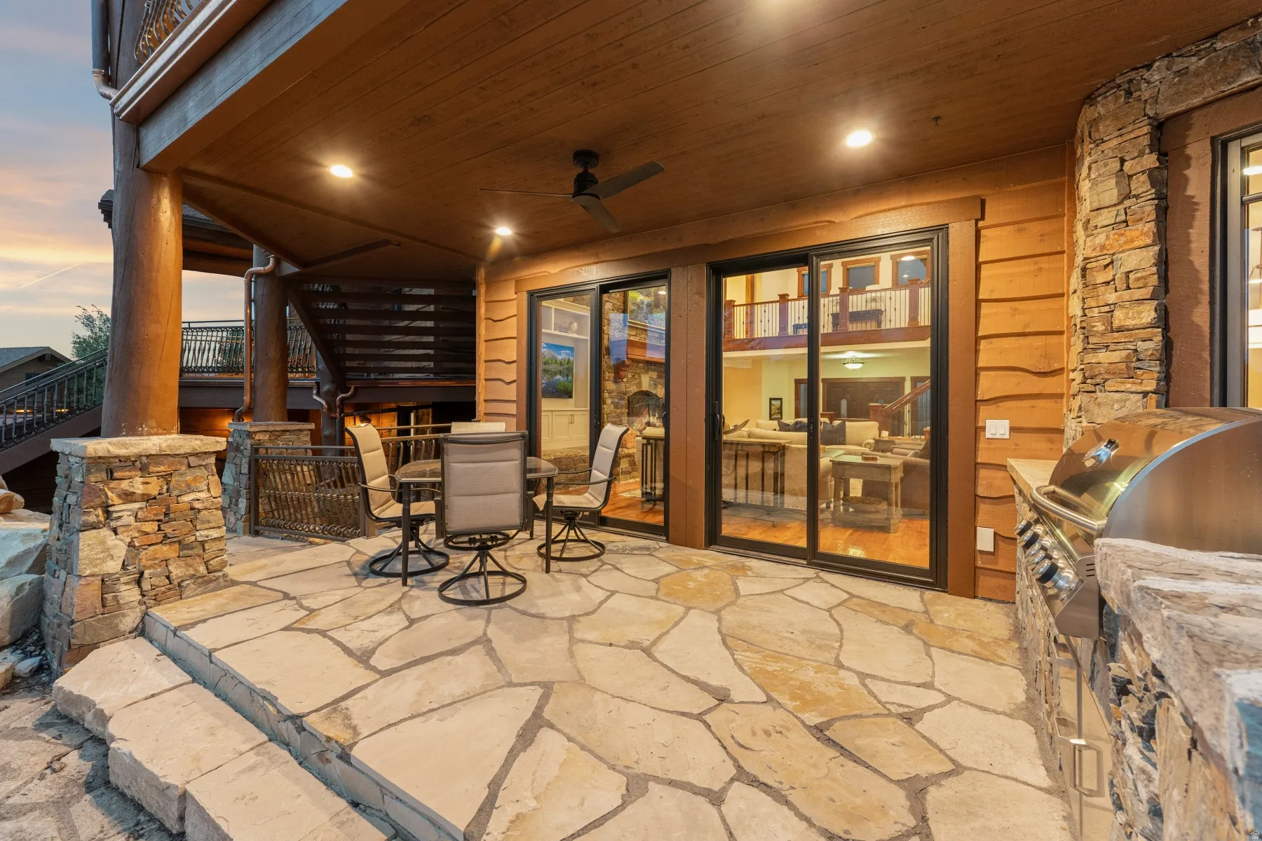 Flagstone patio featuring a built-in outdoor grill, stone column accents, and a wood plank ceiling with recessed lighting