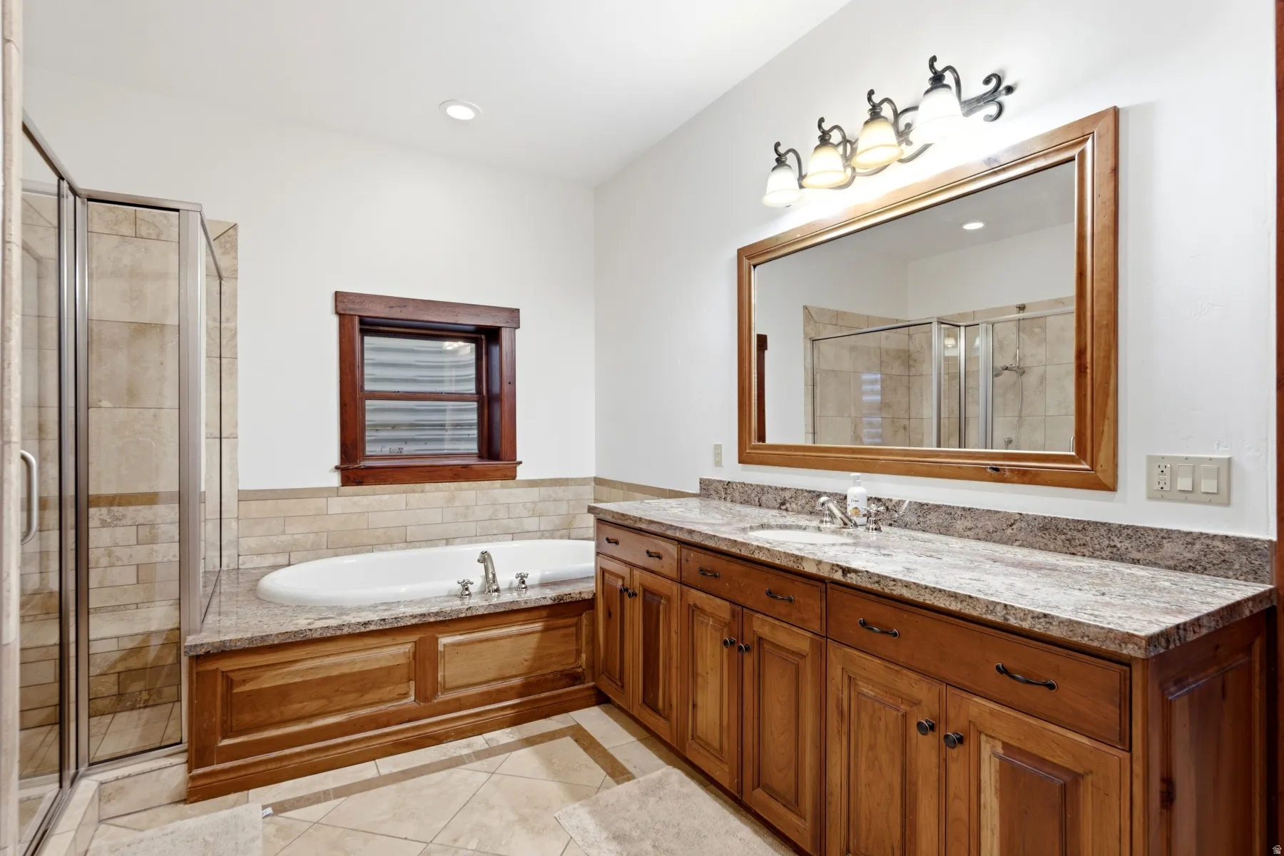 Bathroom featuring an integrated soaking tub, separate glass-enclosed shower, dual basin vanity with stone countertop, and wood-finish cabinetry