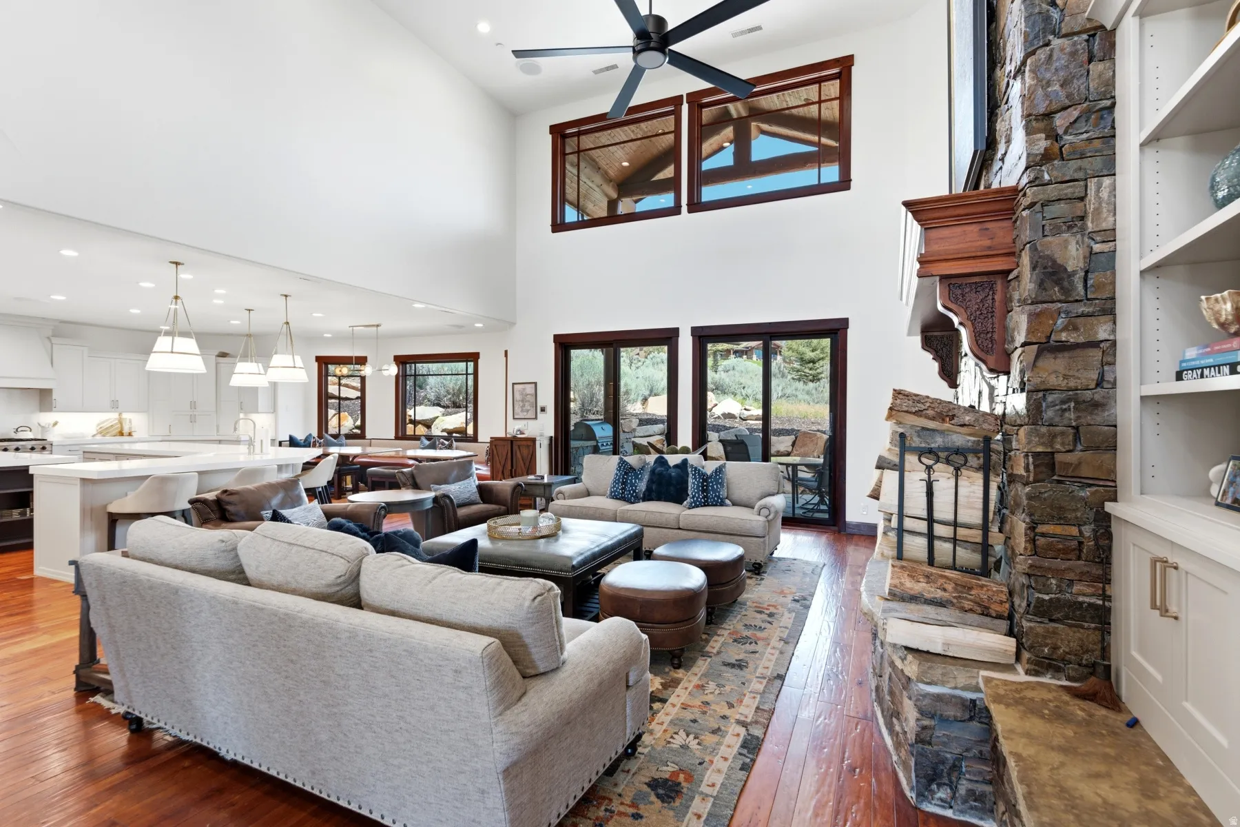Spacious living area featuring high ceilings, wood-finish flooring, and a stone-clad fireplace with an ornate wood mantle