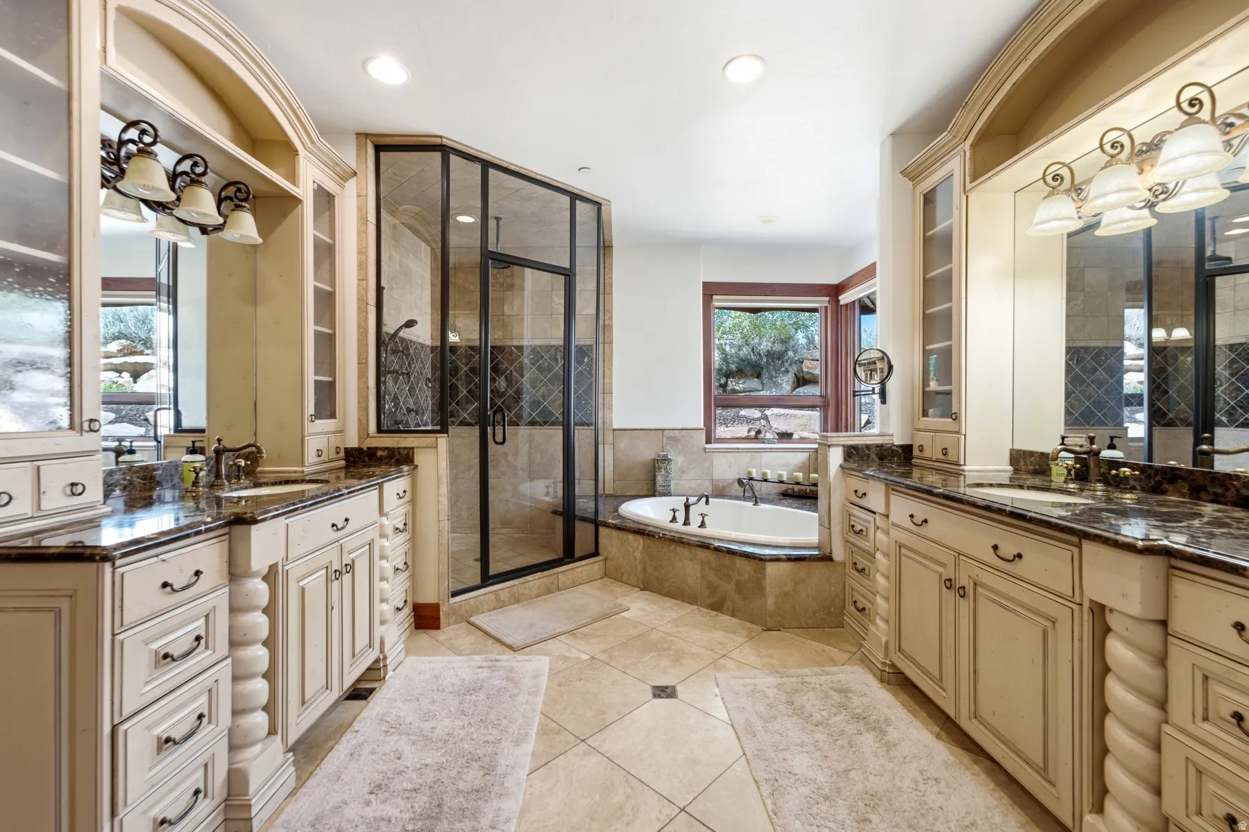Spacious bathroom featuring dual vanities with dark countertops, a walk-in shower with patterned tile, an integrated soaking tub, and tile flooring