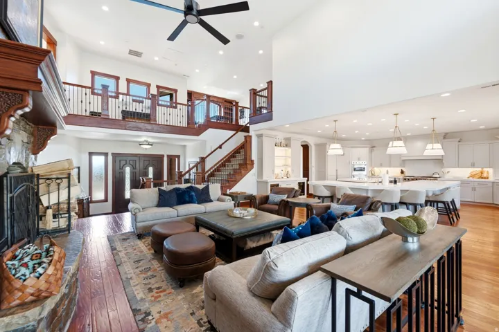 Great room featuring high ceilings, wood-finish flooring, a stone fireplace, and a two-story open layout with an upper-level balcony