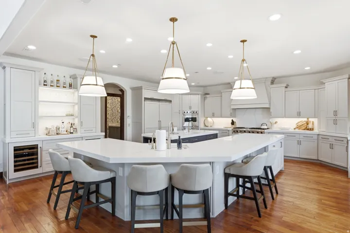Spacious kitchen featuring a large multi-sided island with seating, extensive white cabinetry, integrated wine refrigeration, and hardwood flooring