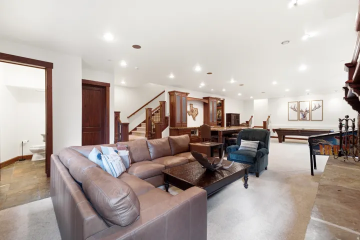 Expansive recreation room featuring recessed lighting, a built-in wet bar with cabinetry, staircase with wood banister, and a stone fireplace hearth