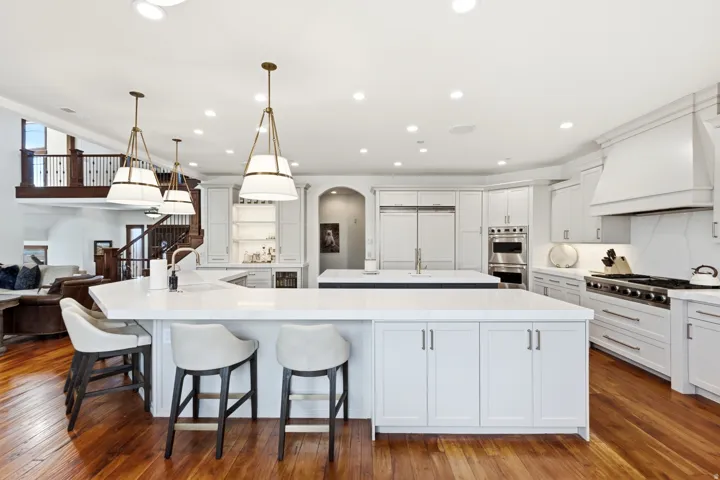 Bright kitchen featuring white cabinetry and light countertops, a large center island, a second island with an integrated sink, a built-in range with a custom hood, and wood-finish flooring