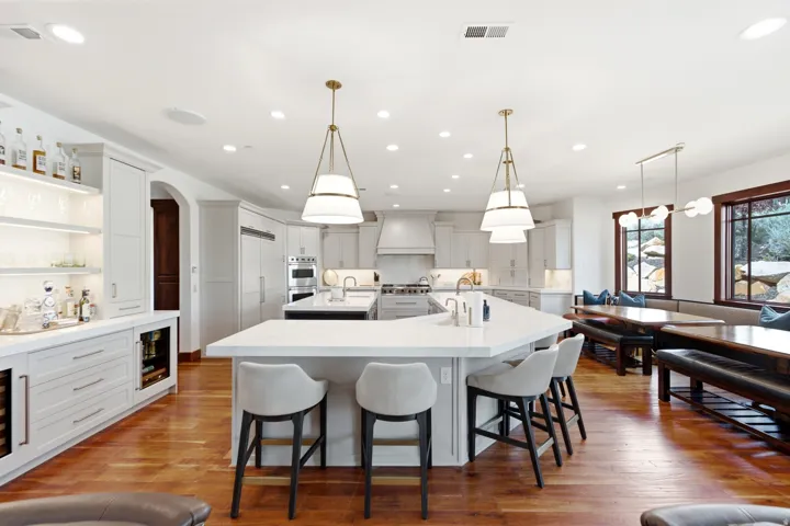 Spacious kitchen featuring an expansive island with seating, a built-in wet bar with beverage refrigerators, recessed and pendant lighting, hardwood flooring, and a breakfast nook with built-in bench seating