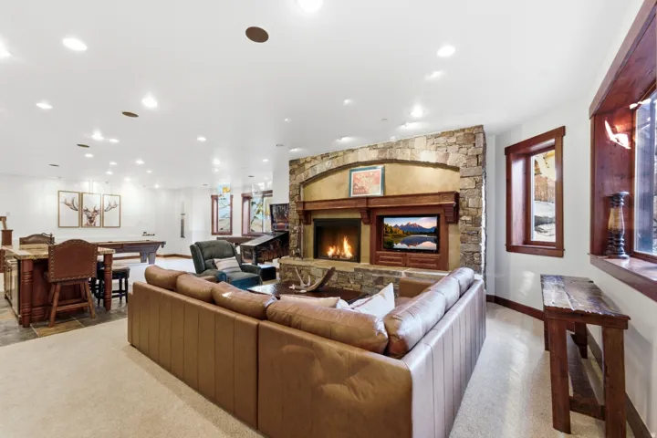 Spacious entertainment room featuring a stone-clad fireplace with a built-in media center, rich wood-trimmed windows, recessed lighting, and a billiards area with a built-in bar