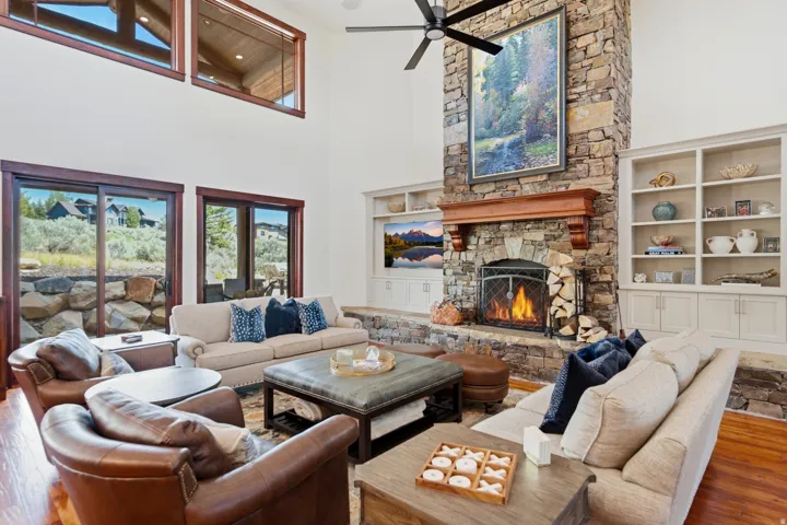 Spacious living area featuring a floor-to-ceiling stone fireplace, built-in shelving, vaulted ceilings, large windows, and hardwood flooring