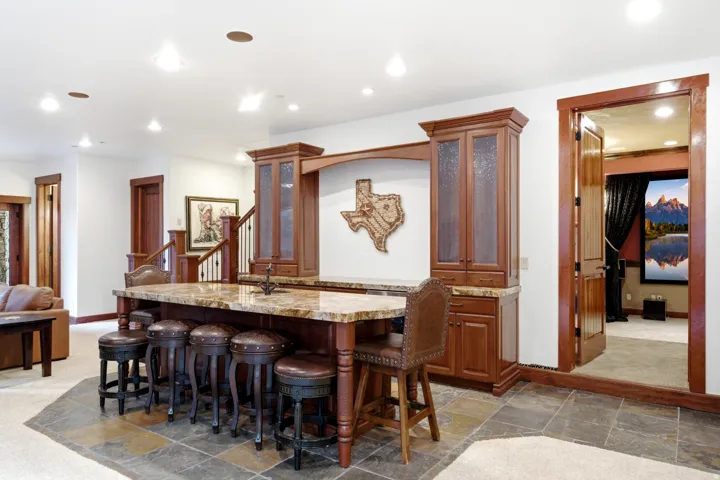 Spacious entertainment area featuring a large center island with seating, a built-in cabinetry unit, natural stone flooring, and recessed lighting