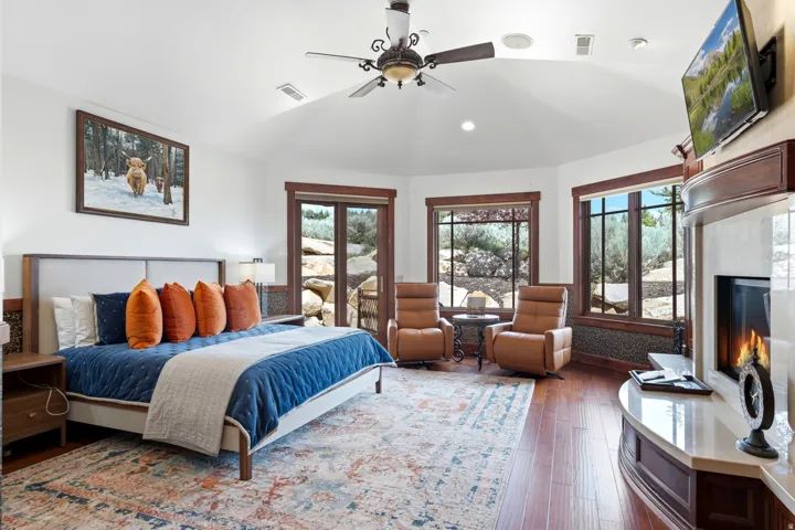 Vaulted ceiling bedroom featuring wood-finish flooring, a built-in fireplace with a stone surround, and multiple windows with exterior views