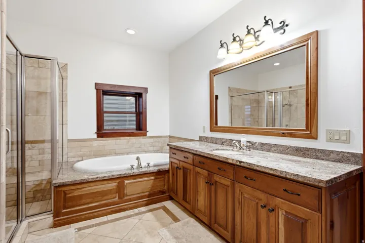Bathroom featuring an integrated soaking tub, separate glass-enclosed shower, dual basin vanity with stone countertop, and wood-finish cabinetry
