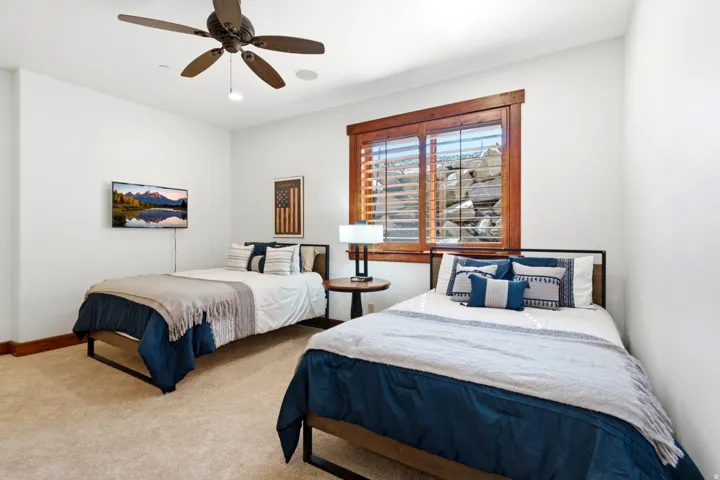 Carpeted room featuring a ceiling fan, a wall-mounted television, and a window with wood blinds and trim