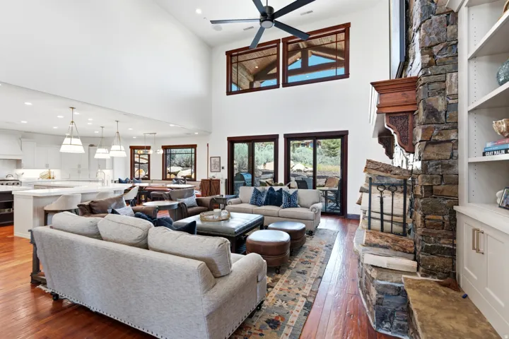 Spacious living area featuring high ceilings, wood-finish flooring, and a stone-clad fireplace with an ornate wood mantle