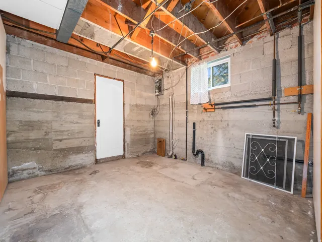 Unfinished basement featuring exposed wood joists, concrete block walls, and a concrete floor