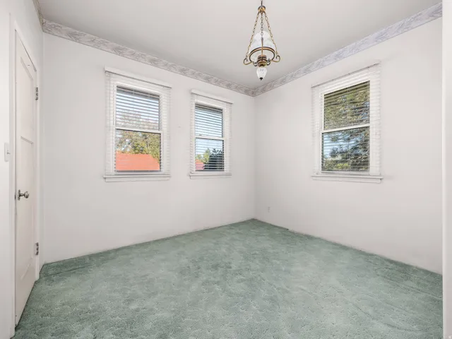 Bedroom featuring three windows with blinds, a ceiling-mounted light fixture, and green carpet