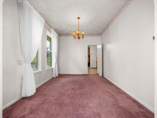 Spacious room featuring two large windows, a central brass chandelier, and a plush purple carpet
