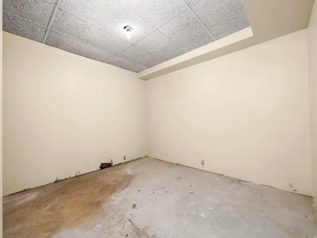 Room featuring light-colored walls and a drop-tile ceiling with an exposed light fixture