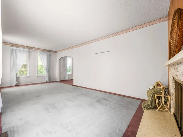 Spacious interior featuring light gray carpeting with a contrasting red border, an arched doorway, and multiple windows providing natural illumination