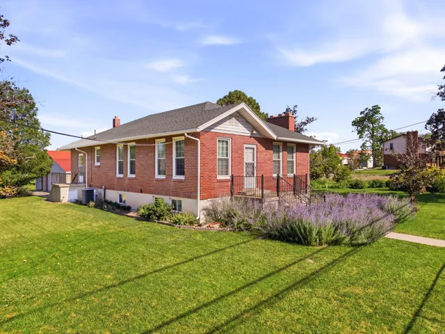 Brick exterior residence featuring a front porch with black railings, a full-light entry door, and perimeter landscaping with purple flowering plants