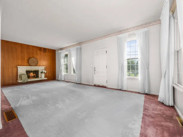 Spacious living area featuring a decorative stone fireplace, wood-paneled accent wall, and multiple windows