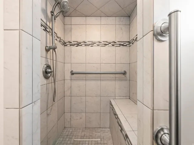 Tiled shower enclosure featuring a mosaic accent band, built-in bench, and a brushed nickel shower system with a hand shower