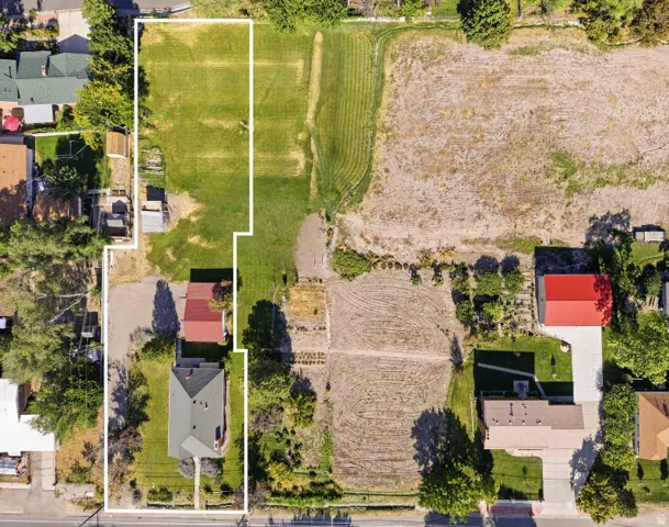 Expansive land parcel featuring a mix of cultivated and uncultivated ground, mature trees, and a residential structure with a light-colored roof