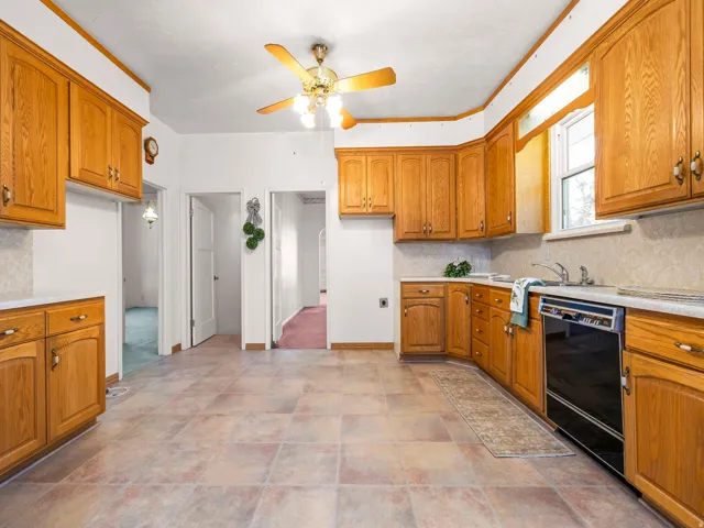 Kitchen featuring wood cabinetry, a built-in dishwasher, tile flooring, a window, and a ceiling fan with integrated lighting