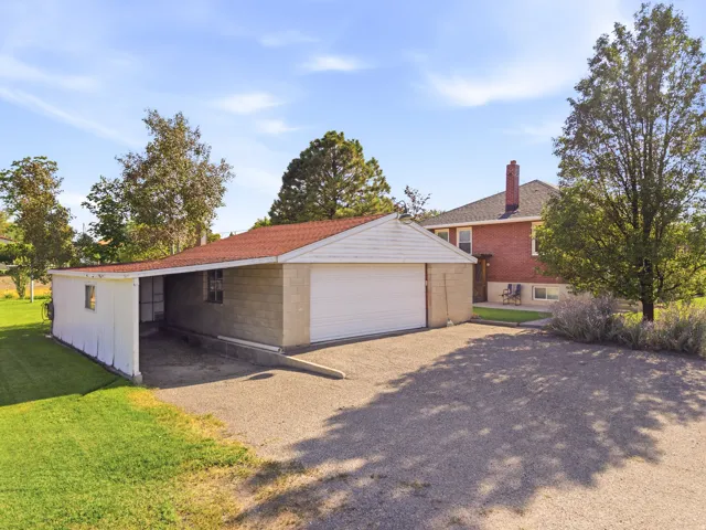 Detached garage with white roll-up door, an attached carport, and a gravel driveway