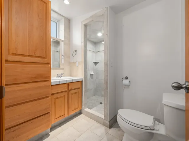 Bathroom featuring a glass-enclosed shower, wood-finish cabinetry, a white tile countertop, and a single vanity