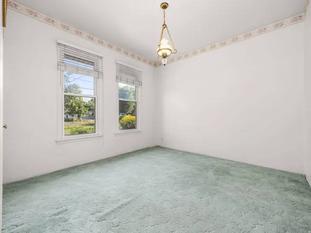 Room featuring light green carpeting, white walls with decorative wallpaper border, and two double-hung windows with blinds
