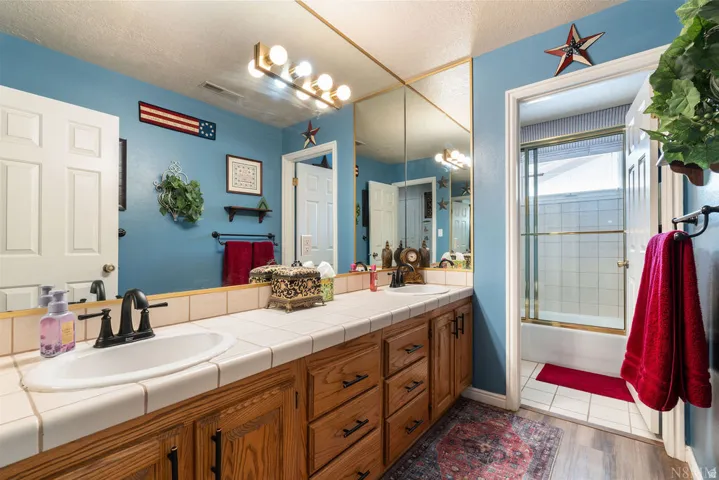 Bathroom featuring an extended vanity with dual sinks, tile countertop, and wood-finish cabinetry