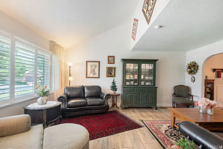 Bright living space featuring vaulted ceilings, plantation shutters, wood-finish flooring, and an arched doorway