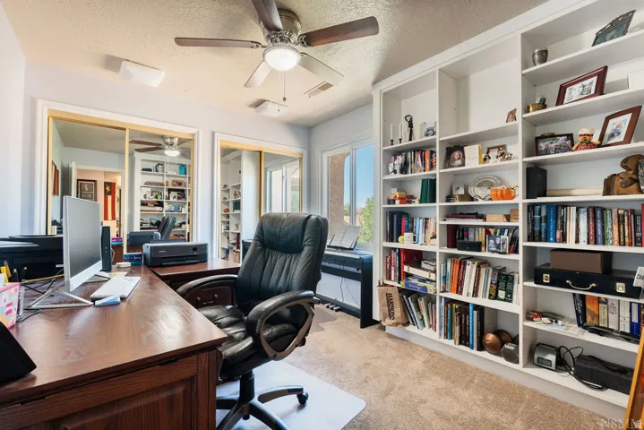 Dedicated workspace featuring a built-in shelving unit, wood-finish desk, and a ceiling fan with integrated lighting