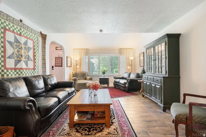 Living area featuring wood-finish flooring, a decorative archway, and a window with plantation shutters
