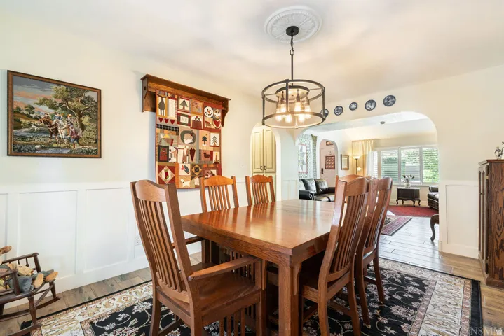 Dining area featuring wainscoting, wood-finish flooring, and an archway leading to an additional living space