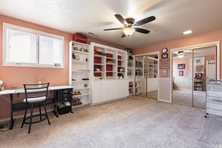 Spacious room featuring extensive built-in shelving, two large windows, a ceiling fan with integrated lighting, and mirrored closet doors